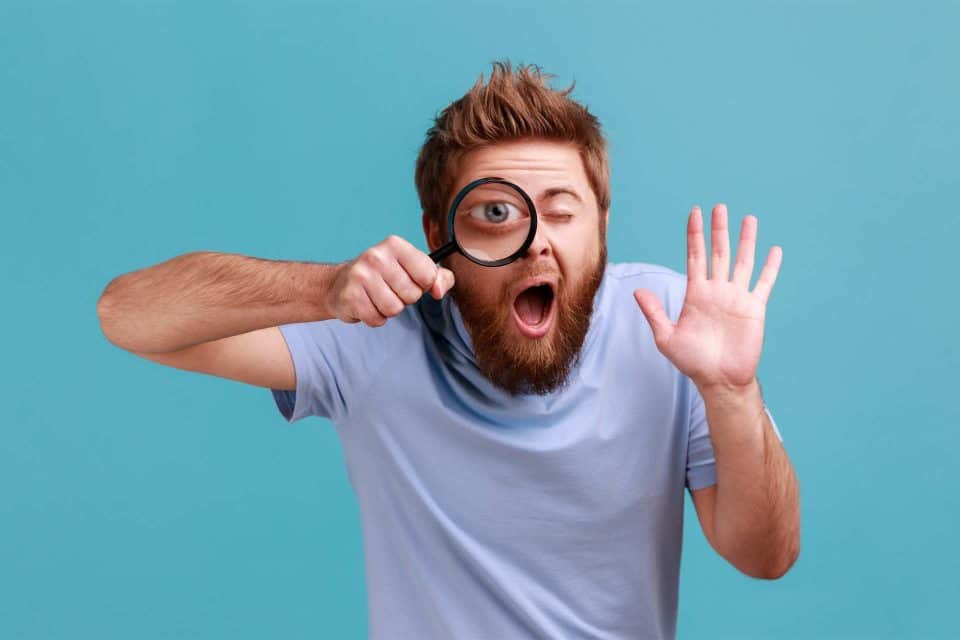 Bearded man with magnifying glass, highlighting brand message, blue background.