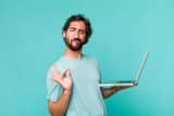 Man in a light blue shirt holding a laptop, making an OK gesture for digital marketing.