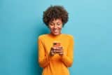 Smiling person in orange sweater using smartphone for digital marketing keywords.