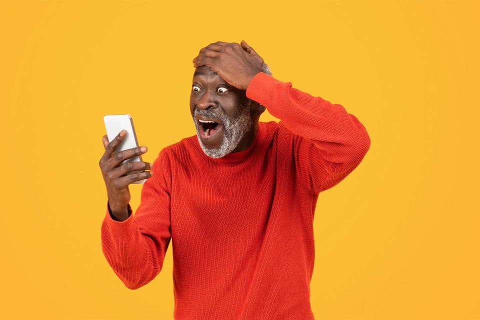 Man in red sweater looks surprised using social listening on smartphone.