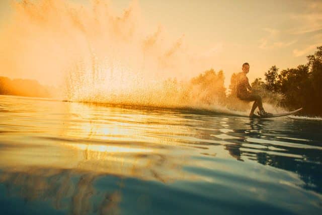 Person wakeboarding on a lake at sunset with water spraying behind them.