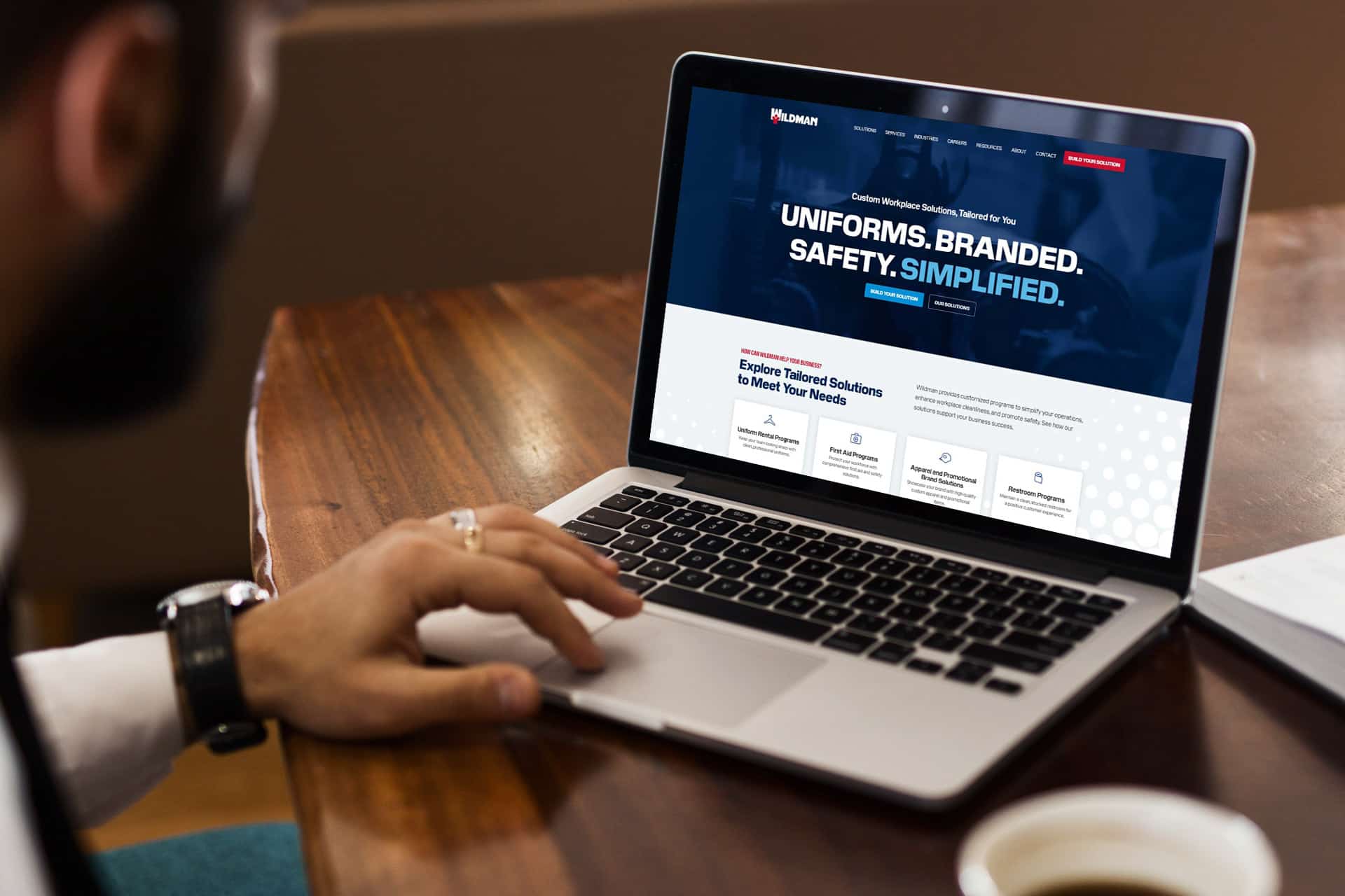 Person using a laptop displaying a website about custom branded uniforms.