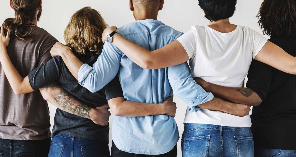 5 people with their arms around each other to show a sense of community.
