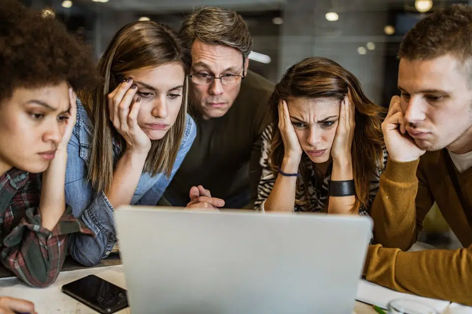 Group of 5 people staring at a laptop computer with frustrated expressions because they're wondering why no one likes my Facebook post.