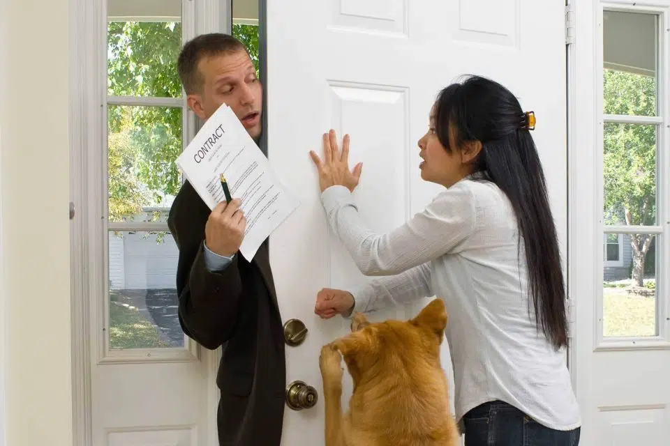 Woman trying to close her front door while a salesman hands her a contract.